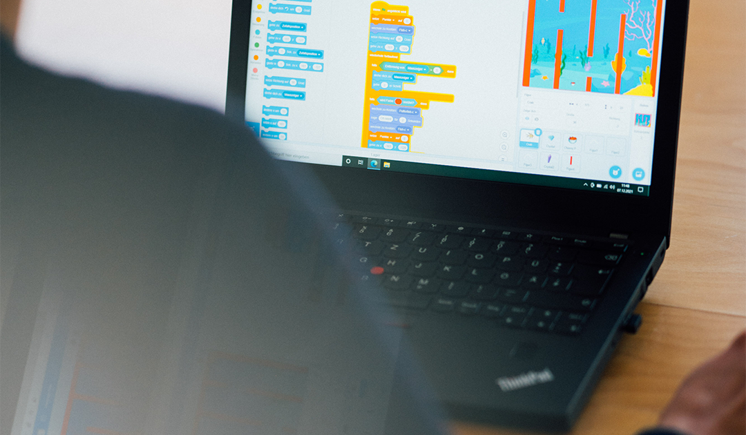 Beim Coden Foto von einem mobilen Rechner. Der Monitor zeigt die Ansicht von Schnipseln einer Programmiersprache