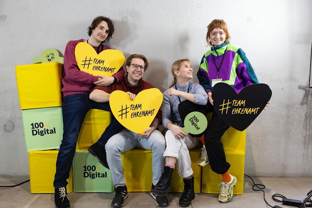 Foto von vier junge Personen, die Schilder mit einem Herz mit dem Text #TeamEhrenamt halten.