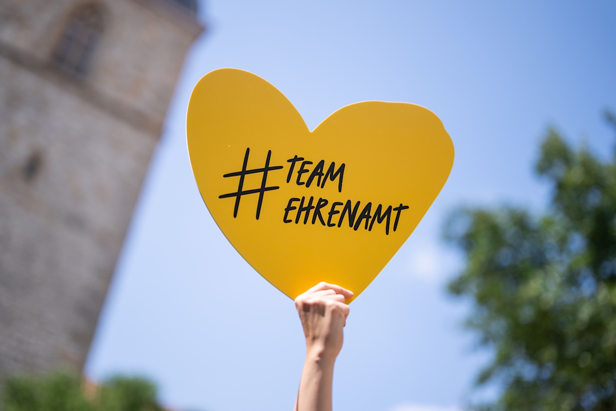 Eine Hand hält ein Schild in Herzform hoch mit dem Text #TeamEhrenamt