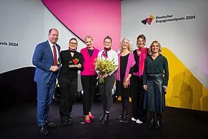 Deutscher Engagementpreis 2024 Personen der Organisation Kieler Brustkrebssprotten e.V. auf einer Bühne mit Verena Bentele und Jan Holze
