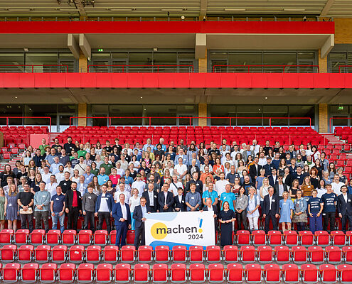 Gruppenbild auf der Stadiontribüne "An der alten Försterei" in Berlin mit den vielen engagierten Vertretern:innen der Preisträger des Machen!2024 Wettbewerbs.