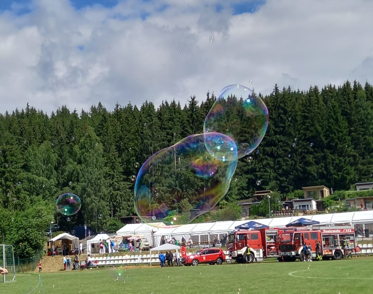 Seifenblasen schweben über einem Fußballplatz. Im Hintergrund stehen Feuerwehrautos. Foto des ELa-Netzwerks "Miteinander im Kristall des Erzgebirges"