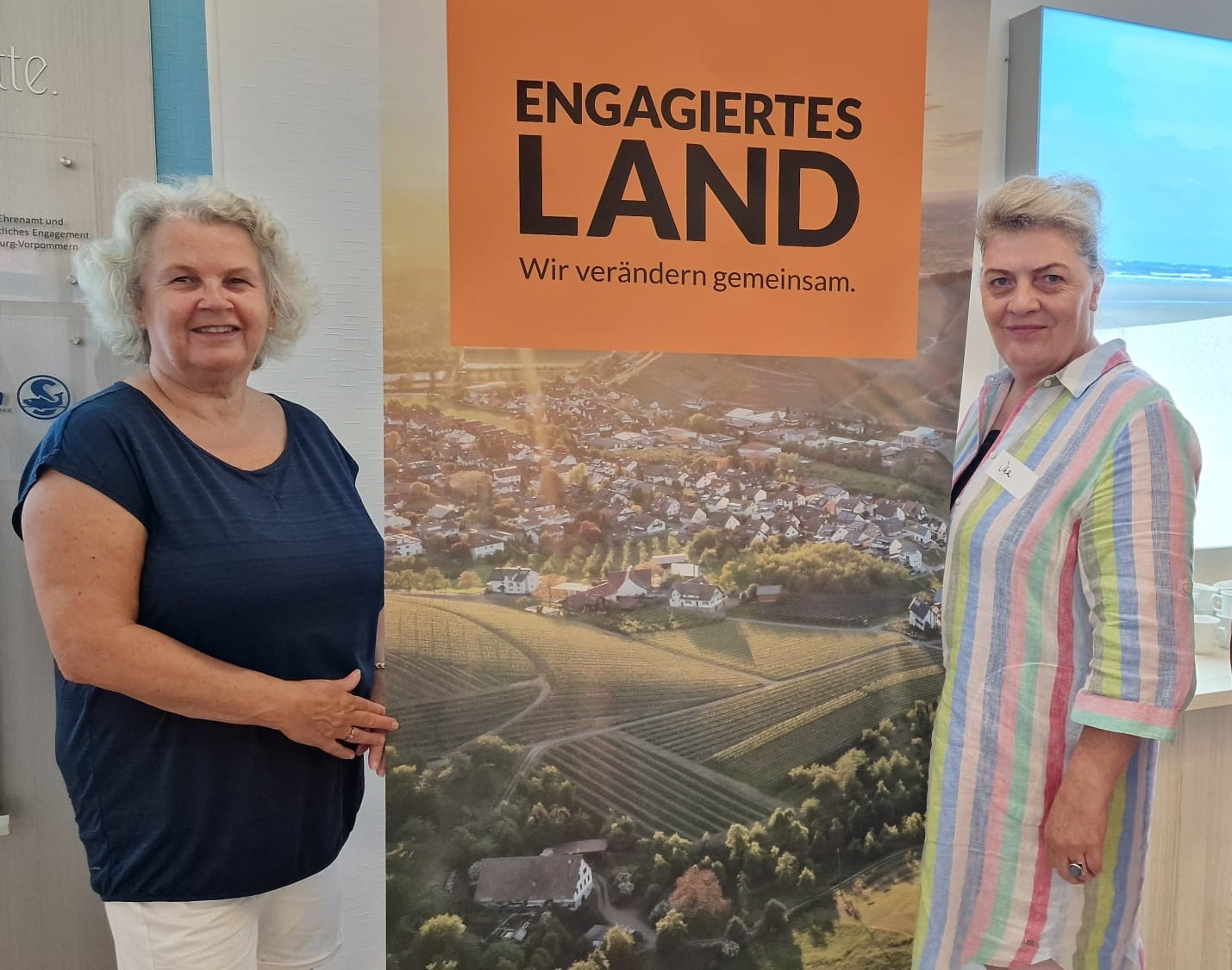 Zwei Engagierte des Netzwerks Schwaan stehen vor einem ELa-Plakat